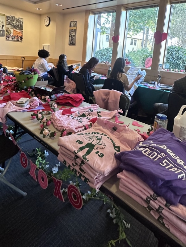 Valentines tea party event image of one of the crafting tables with pink and purple  donated vintage Humboldt state t-shirts free to decorate and upcycle , students in the background decorating valentines gifts